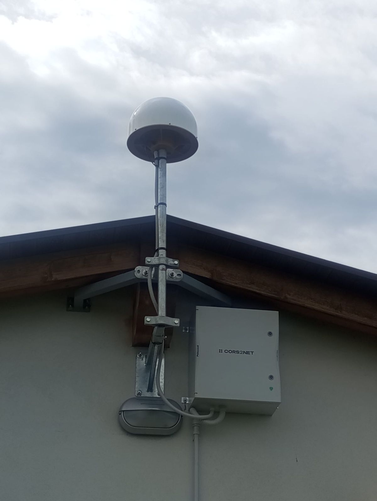 StarCORS reference station: choke ring GNSS antenna on a mast with its equipment enclosure, mounted on a building